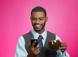 Closeup portrait happy, smiling business man reading good news on smart phone, lawyer holding mobile, drinking cup coffee isolated pink background. Human face expression, emotion, corporate executive