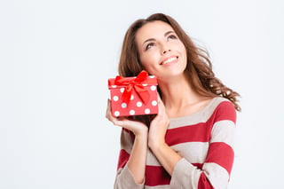 Portrait of a happy thoughtful woman holding gift box and looking up isolated on a white background.jpeg