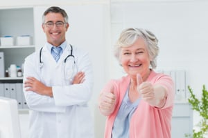 Portrait of happy female patient showing thumbs up sign while standing with doctor in clinic