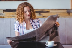 Pretty curly hair girl having cup of coffee and reading newspaper at the cafe-1