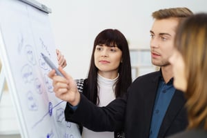 Young businessman having a serious discussion with two female co-workers as they stand together discussing a hand written flip chart