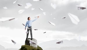 Young businessman on rock top with paper plane in hand